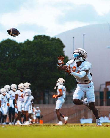Football player reaching to catch a ball during practice.