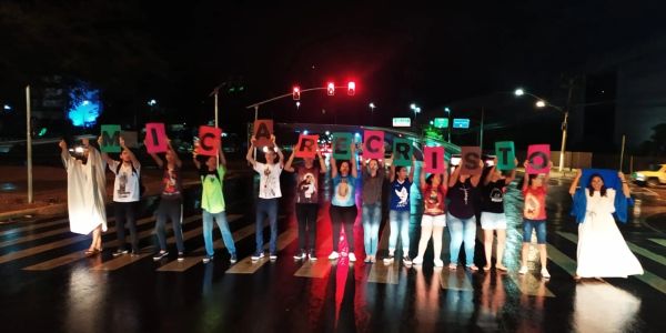 Group holding colorful letters spelling a message at night on a crosswalk.