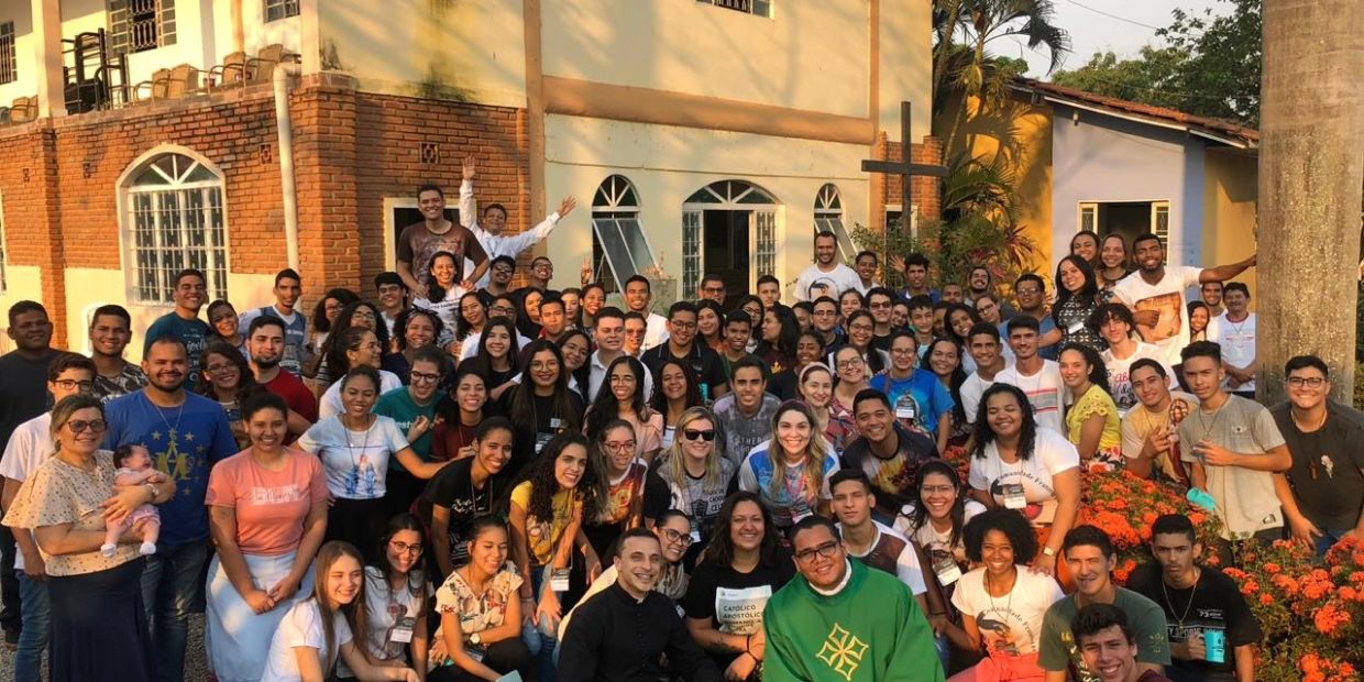Large group of people posing together outside a building with a cross.