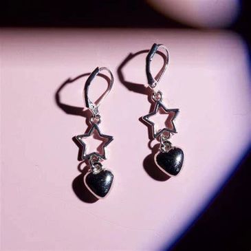 Silver earrings with star and heart designs on a pink background.