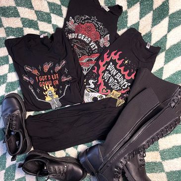 A collection of black graphic tees and black boots on a green checkered background.