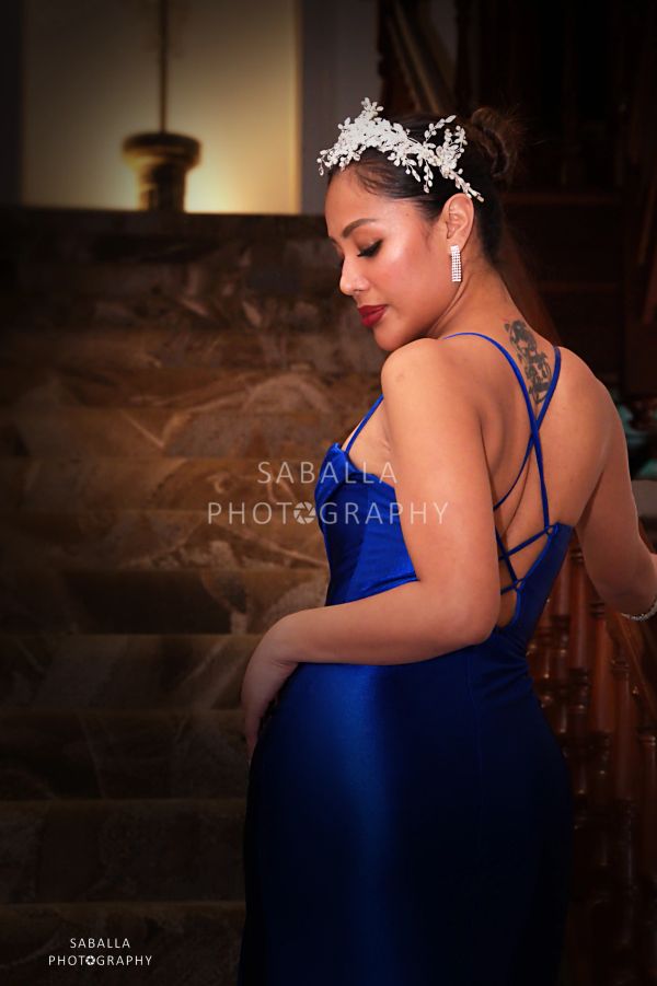 Woman in a blue dress with floral headpiece poses on stairs.