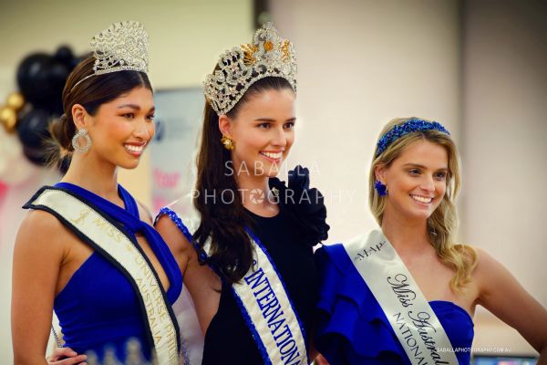 Three beauty queens wearing crowns and sashes, smiling.