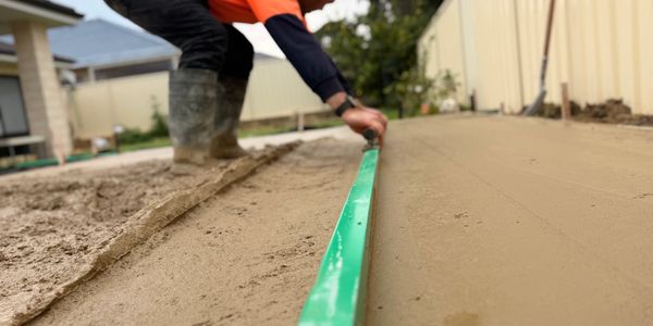 Worker leveling freshly poured concrete with a green screed tool.