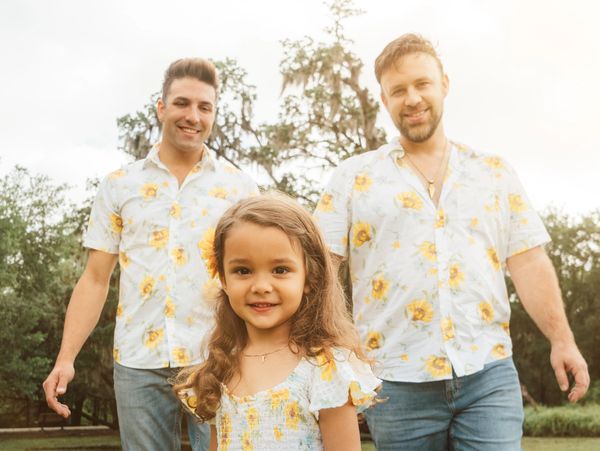 A young girl with two men in matching floral shirts outdoors.