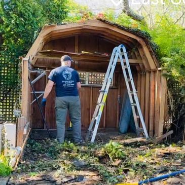 Man dismantling a wooden shed in a garden.