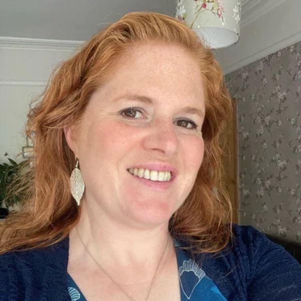 Smiling woman with red hair and leaf-shaped earrings in a cozy room.