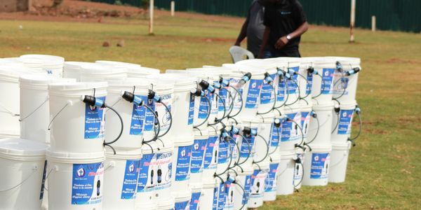 Rows of white water filtration buckets with taps outdoors.