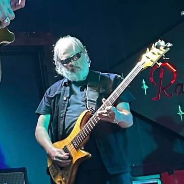 An older man with sunglasses playing an electric guitar on stage.