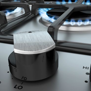 Close-up of gas stove knob and burner with blue flame.