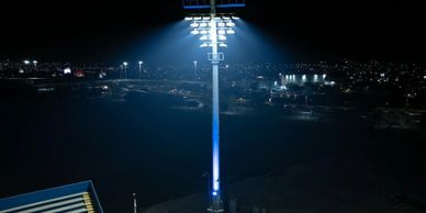 A tall stadium floodlight tower illuminated against a dark night sky.