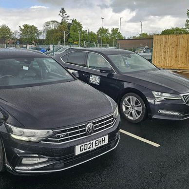 Two black sedans parked side by side in an outdoor lot on a cloudy day.