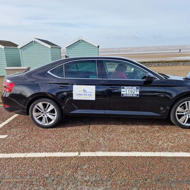 Black sedan parked near beach huts with signs on doors.