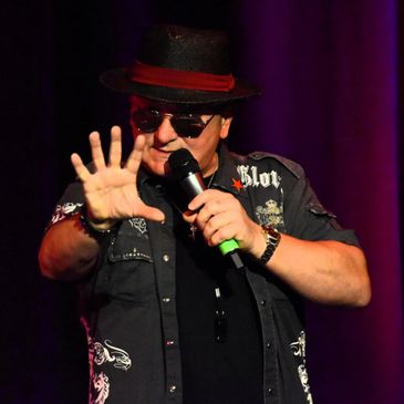 Male performer in sunglasses and hat holding a microphone on stage.