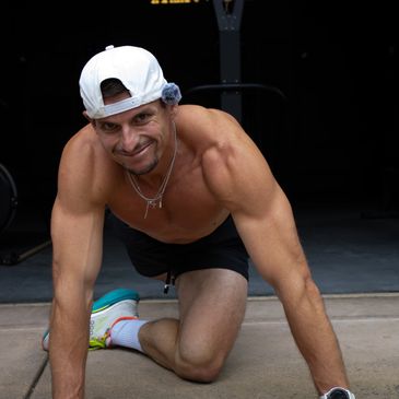 Smiling man in workout gear poses on floor, showing muscular arms.
