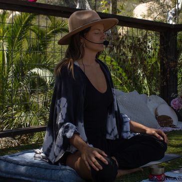 Woman meditating outdoors wearing a hat and microphone headset.