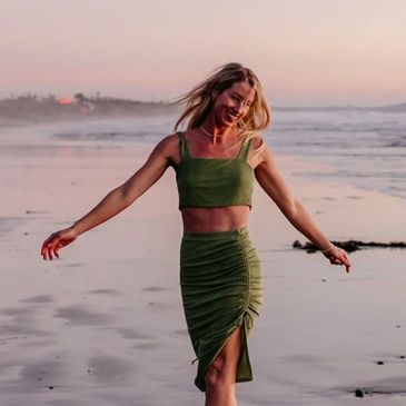 Woman in green dress joyfully walking on the beach at sunset.