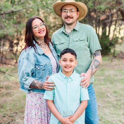 A smiling family of three posing outdoors in casual clothing.