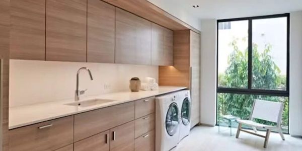 Modern laundry room with wooden cabinets, washer and dryer, and large window.