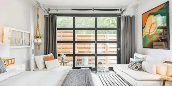 Bright modern bedroom with large glass garage-style door and cozy seating area.