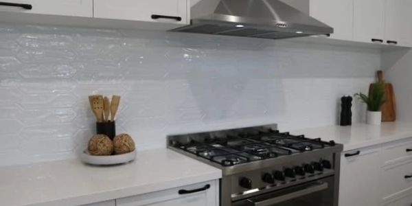 Modern kitchen with white countertops, stainless steel stove, and decorative wooden utensils.
