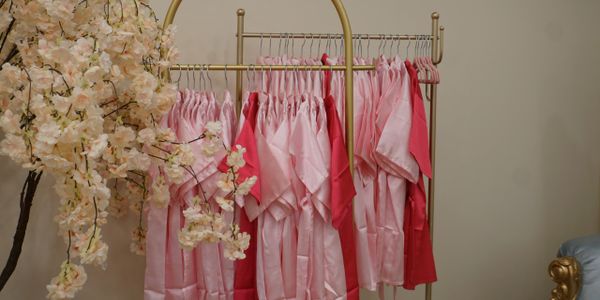 Pink and red robes hanging on a gold clothing rack beside a flowering branch.