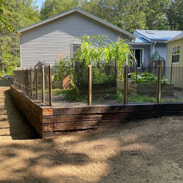 Raised garden beds protected by a glass fence in a backyard.