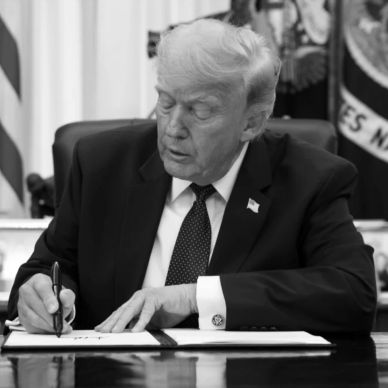 Man in suit signing documents at desk.