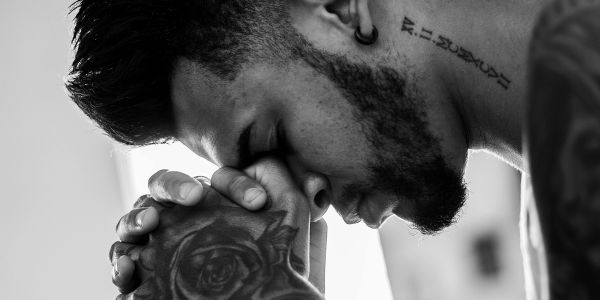 Man with tattoos and earrings in deep thought or prayer, black and white photo.