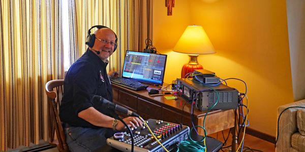 Man wearing headphones operates audio equipment at a desk in a cozy room.