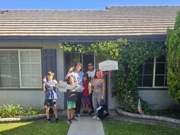A family of five standing in front of their house holding signs with a sold message.