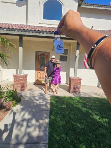 Couple standing in front of their new home, holding keys in foreground.