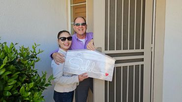 Happy couple holding a 'Sold' sign in front of their new home.