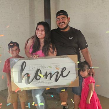 A happy family holding a 'home' sign, celebrating together with confetti.
