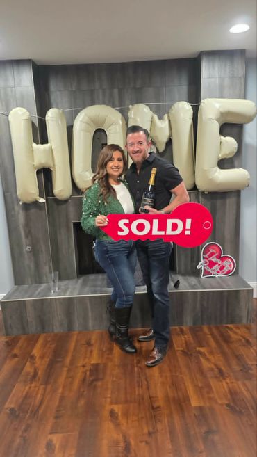 Happy couple celebrating home purchase with SOLD sign and champagne.