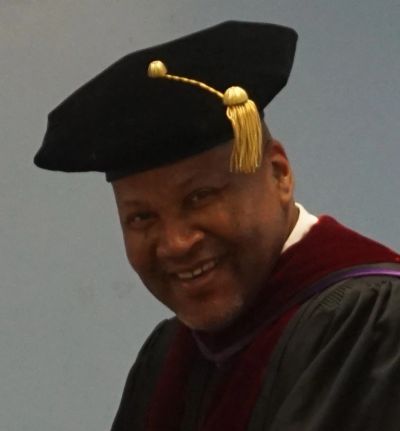 Smiling man in academic regalia with a black cap and gold tassel.
