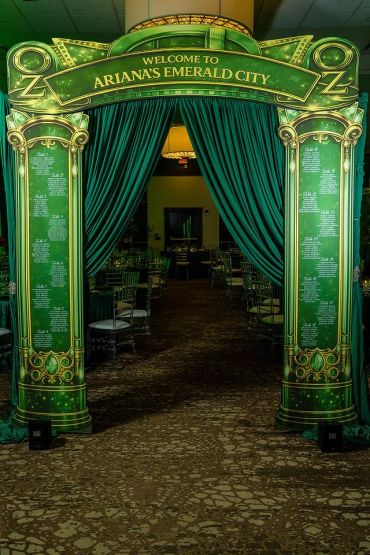 An ornate green archway welcomes guests to Ariana's Emerald City event with detailed seating charts.