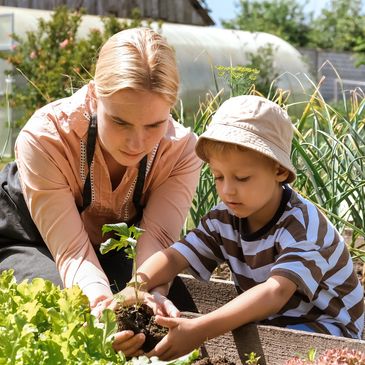 Woman helping a little boy in the garden. Little boy is wearing a bucket hat and a striped shirt. 