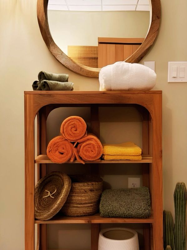 Wooden shelf with neatly folded and rolled towels under a round mirror.