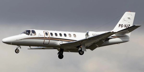 A white private jet in mid-flight against a cloudy sky.