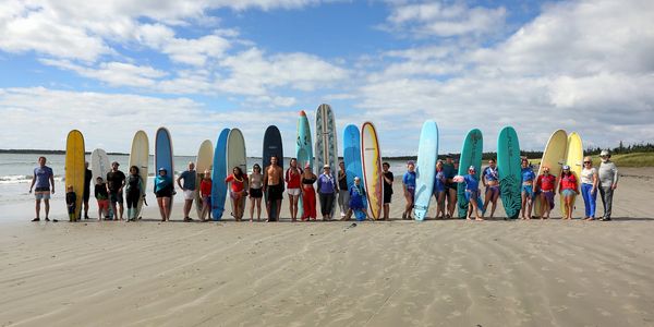 Group of people with surfboards lined up on a beach under a cloudy sky.