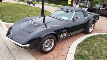 A sleek black vintage convertible sports car parked on a brick pathway.