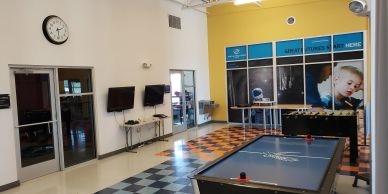 A recreational room with air hockey and foosball tables, yellow and white walls, and checkered flooring.