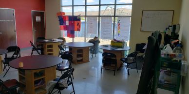 Classroom with round tables, chairs, and colorful decorations near a large window.