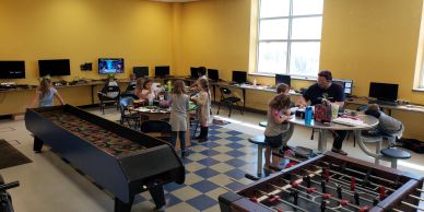 Children playing and relaxing in a brightly lit game room with tables and arcade games.