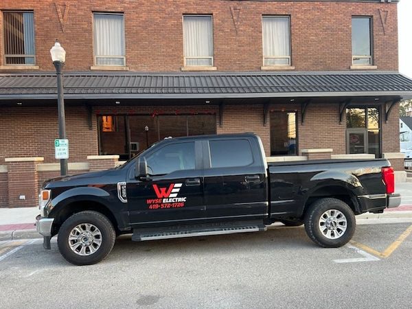 Black pickup truck with Wyse Electric logo parked on street.