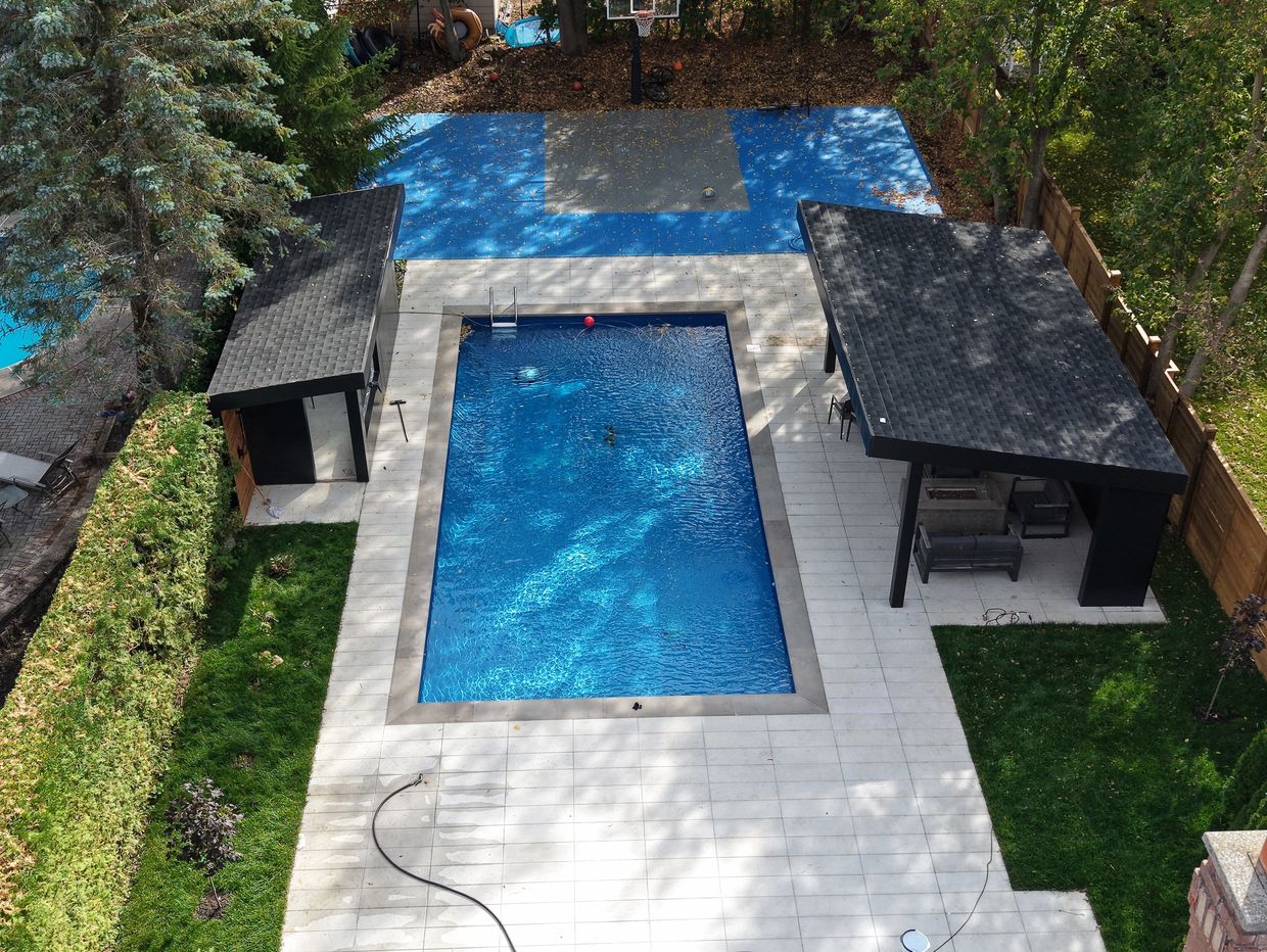 A backyard with a swimming pool, two shaded seating areas, and a basketball court.
