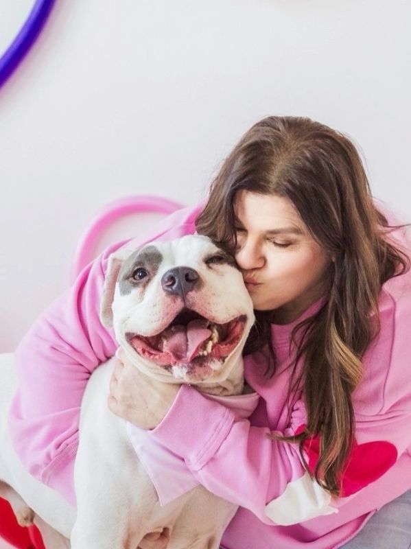 Woman in pink hugs and kisses a happy white dog.