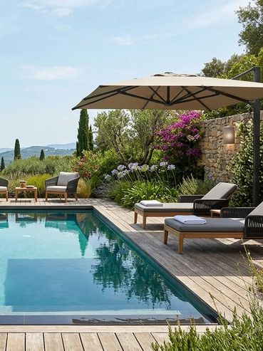 Elegant poolside area with loungers, an umbrella, and lush greenery under a clear sky.