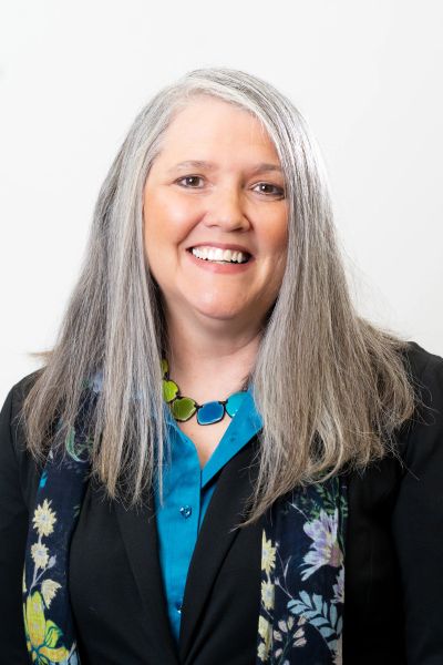 Smiling woman with long gray hair and colorful necklace.